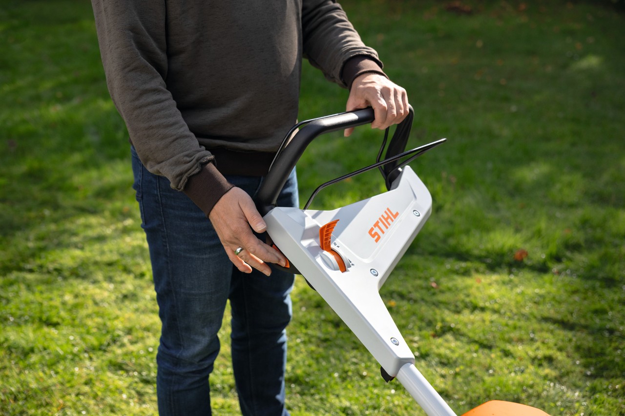 Una persona su un prato preme il pulsante di avviamento di un tosaerba a batteria STIHL