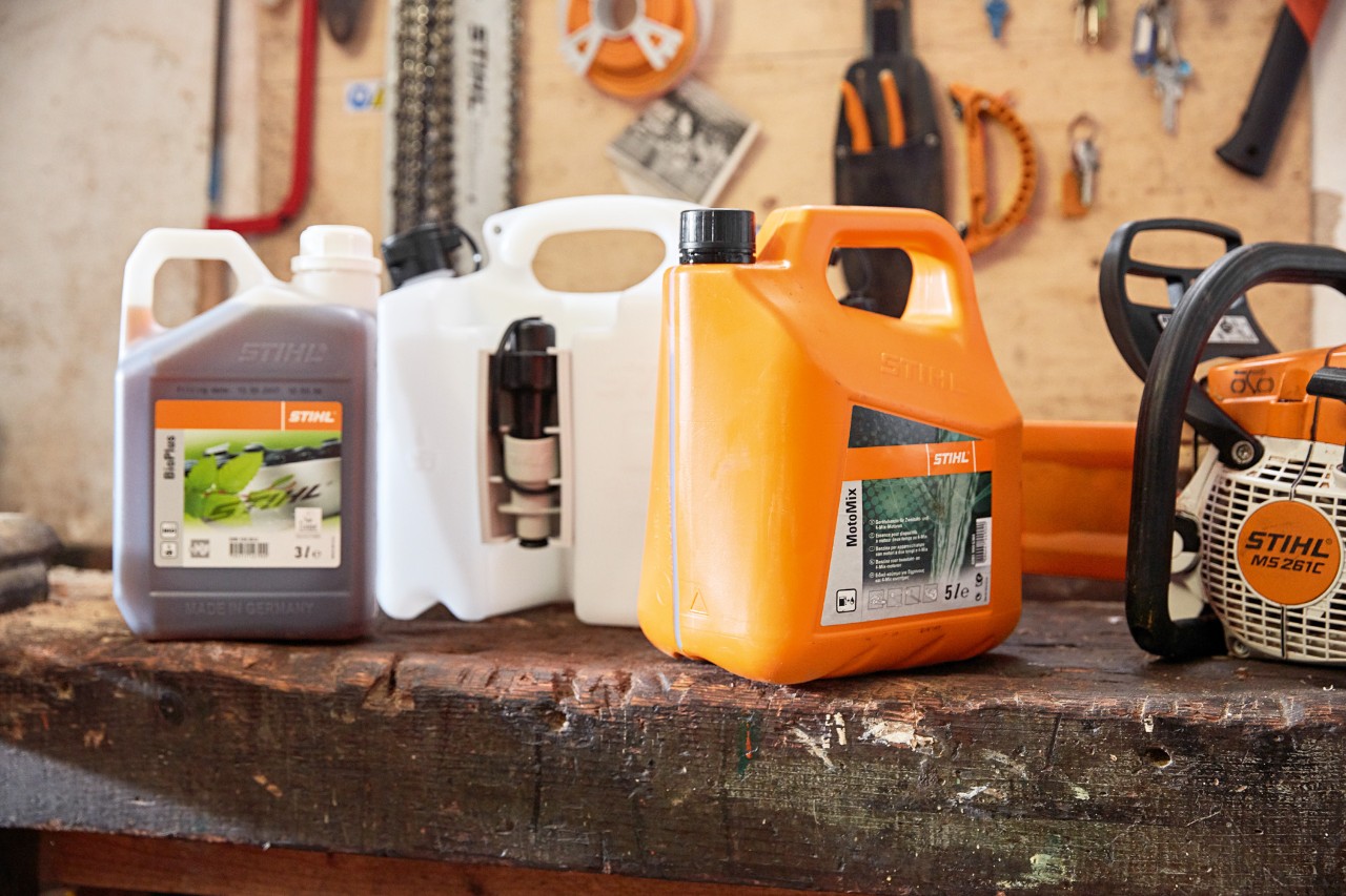 Tanica con miscela di olio e benzina per motoseghe STIHL MotoMix e una motosega a benzina STIHL MS 261 C all'interno di un'officina