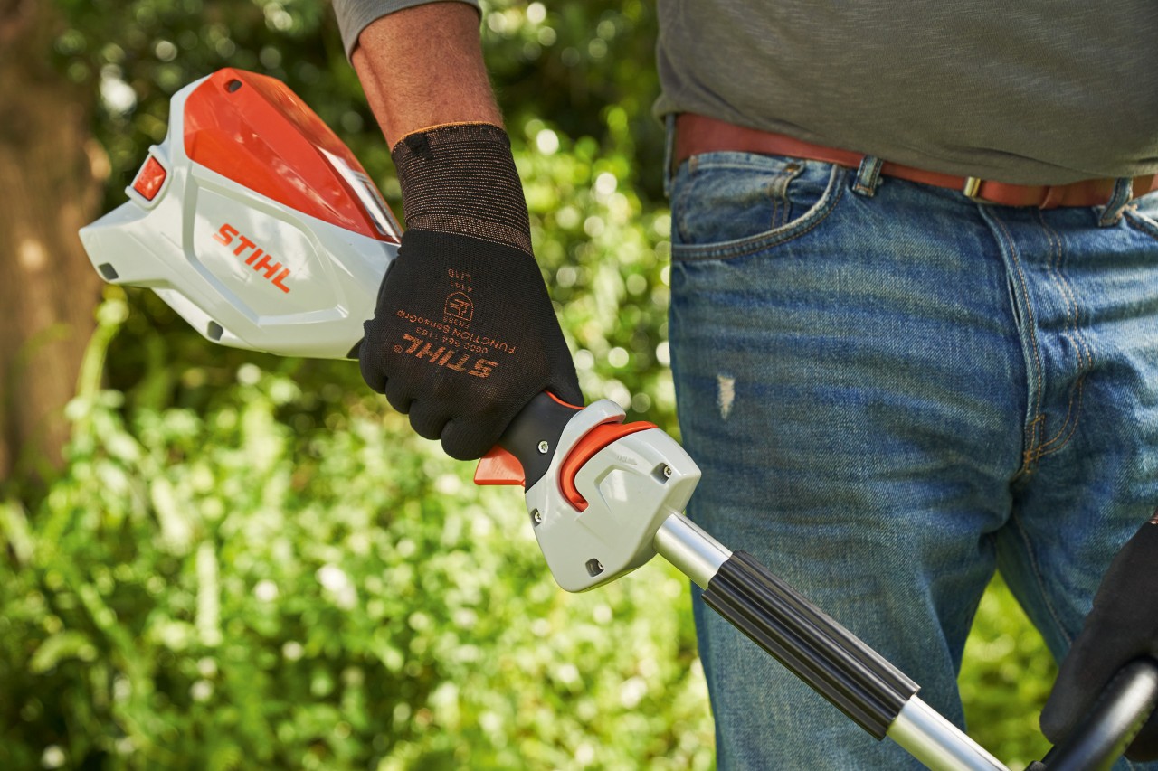 Uomo con guanti di protezione preme il blocco leva del cambio del decespugliatore a batteria STIHL FSA 60 