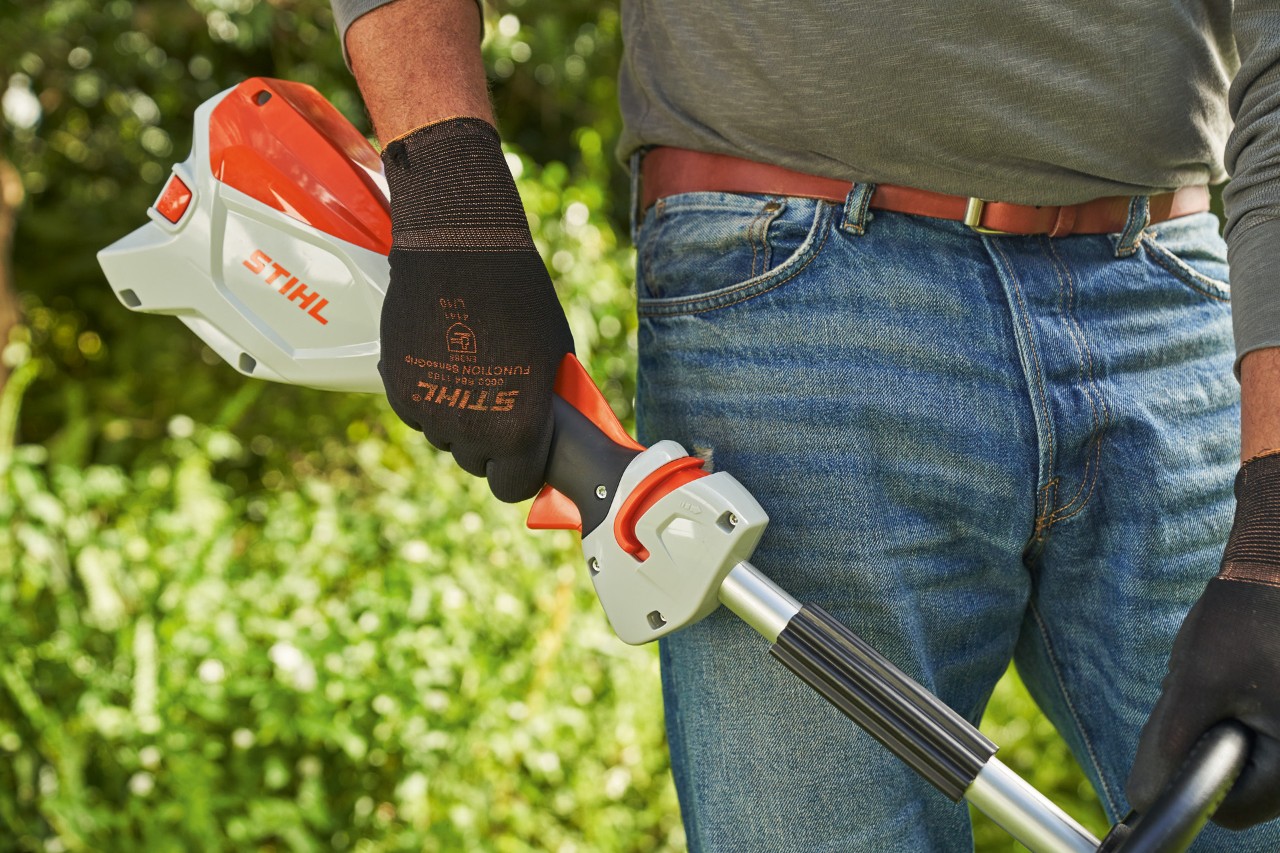 Uomo con guanti protettivi rilascia la leva del cambio del decespugliatore a batteria STIHL FSA 60 per spegnerlo