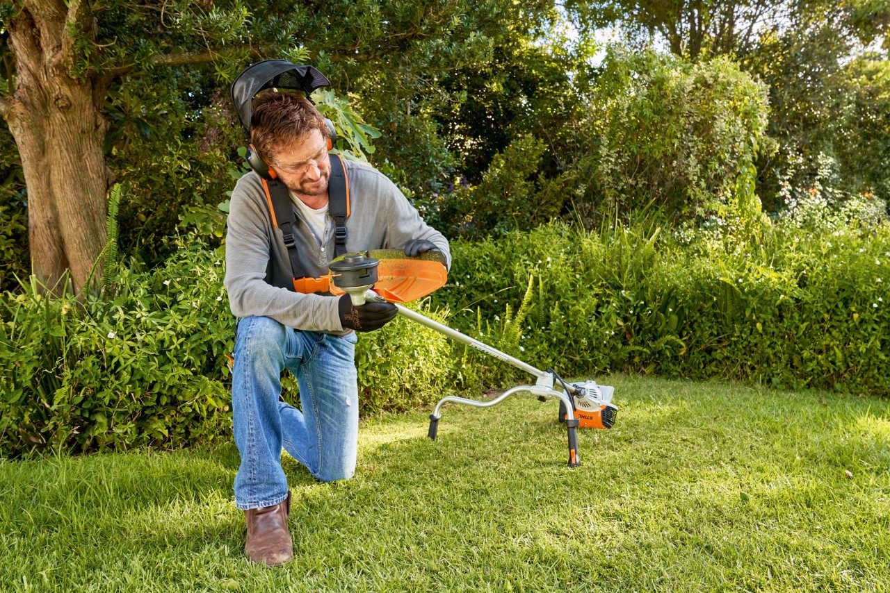 Uomo che prepara un decespugliatore in giardino per sostituire l’utensile da taglio