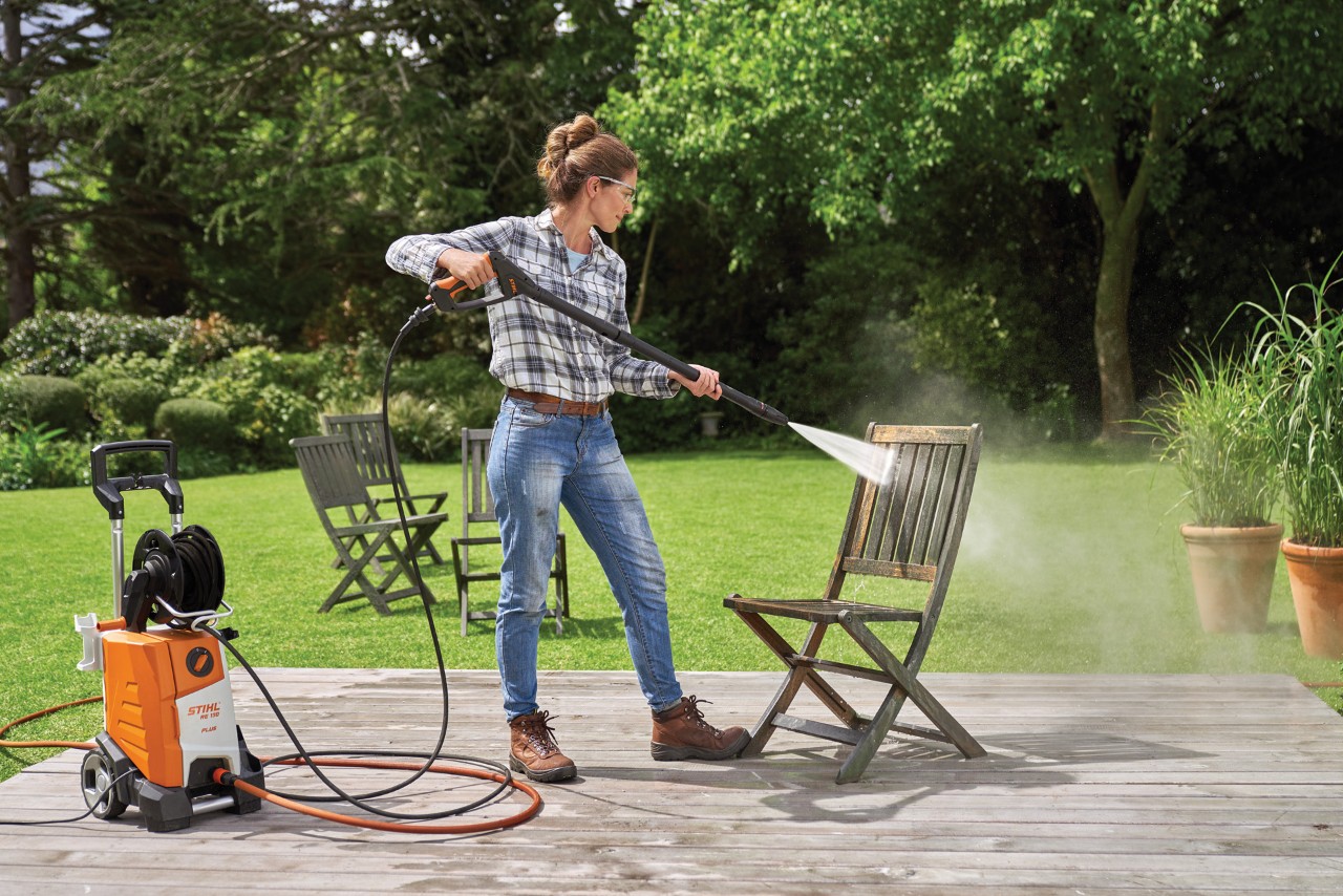 Donna che pulisce un mobile da giardino in legno con un'idropulitrice sul terrazzo