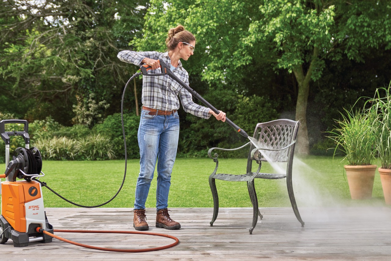 Donna che pulisce un mobile esterno in metallo con l'idropulitrice STIHL RE 130 plus sul terrazzo