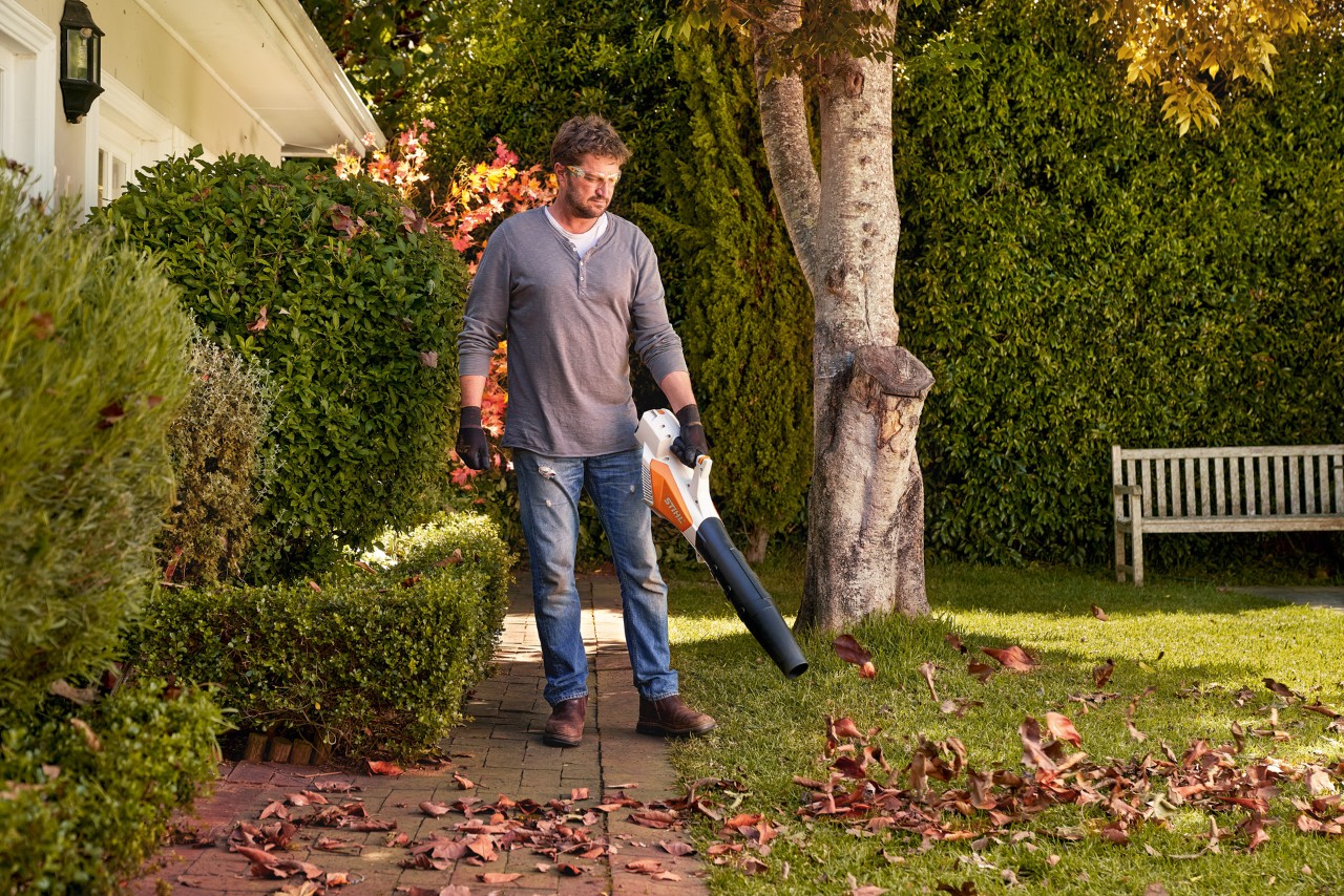 Uomo che pulisce il vialetto in pietra antistante la propria casa con un soffiatore per foglie senza fili STIHL BGA 57.