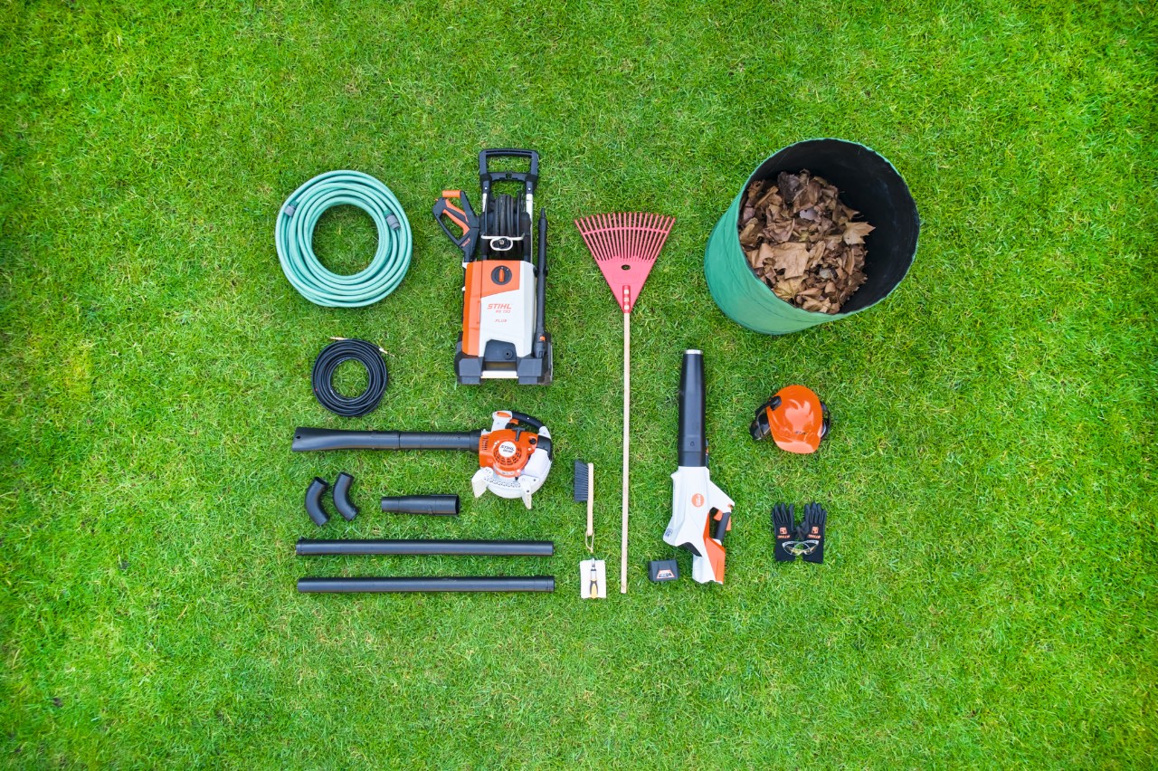 I singoli pezzi del set per la pulizia delle grondaie STIHL sono ordinatamente disposti su un prato, uno accanto all'altro. 
