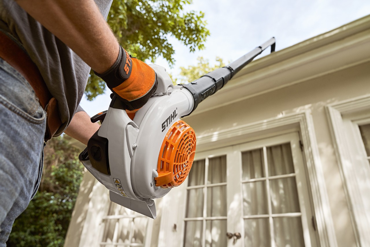 Persona che indossa guanti protettivi mentre pulisce la grondaia di una casa con il set pulizia delle grondaie di STIHL